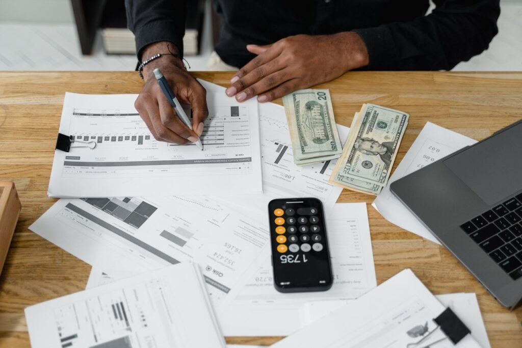 Home Man working on financial reports with calculator, money, and laptop on a desk.