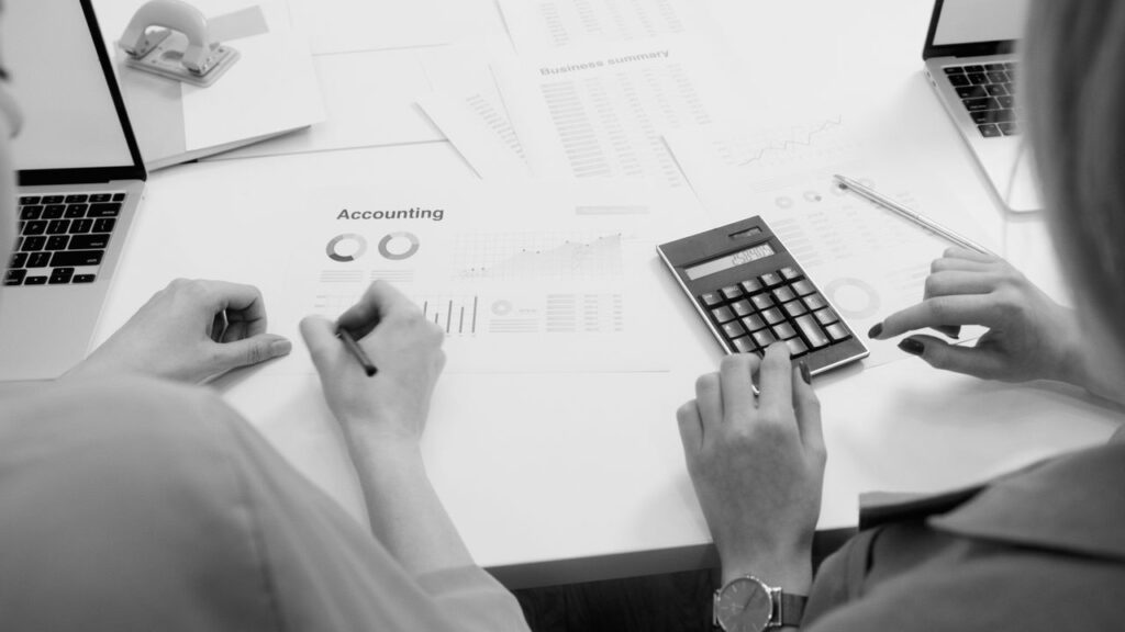 Home Black and white office scene featuring accounting documents, calculator, and laptops.