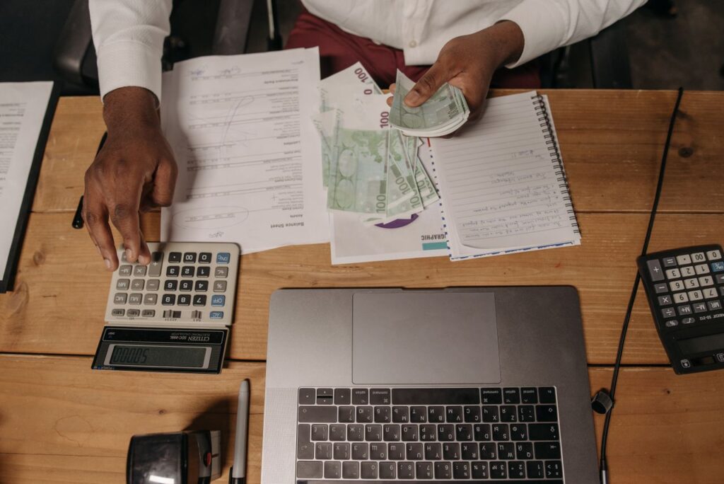 Home Close-up of a person counting cash with documents and a laptop in an office setting.